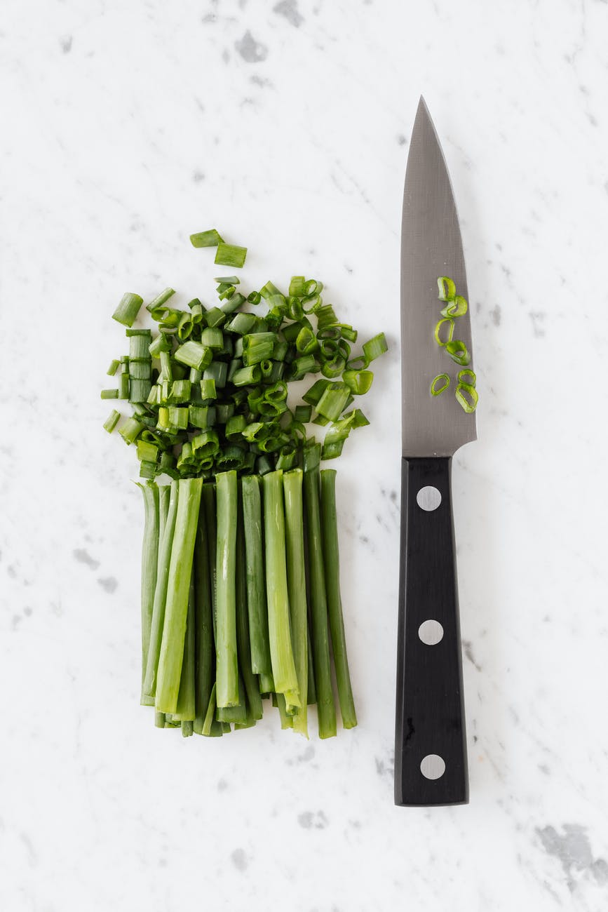 fresh green onion and knife on white table